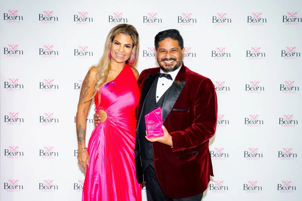 A woman in a fuchsia dress beside a man holding a Beam Awards trophy, a past programme